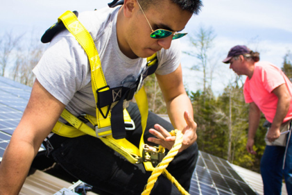 A College of the Atlantic student helps install solar panels on the roof of a local business.